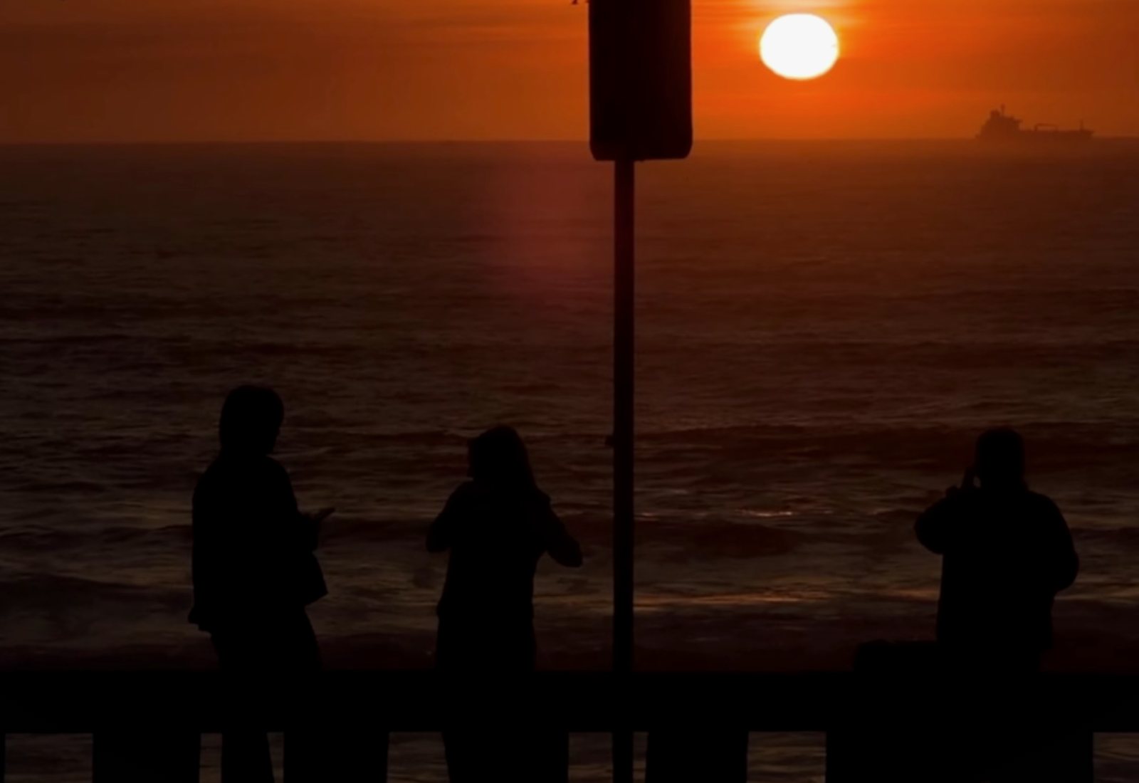 Three people silhouetted against the sunset over the ocean